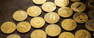 A high-definition, close-up view of various physical golden cryptocurrency coins—including Bitcoin, Ethereum, Dogecoin, and Litecoin—scattered across a dark, textured surface.