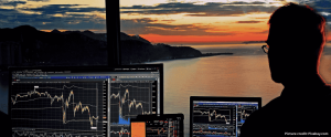 Trader with multiple screens open looking out onto a sunset