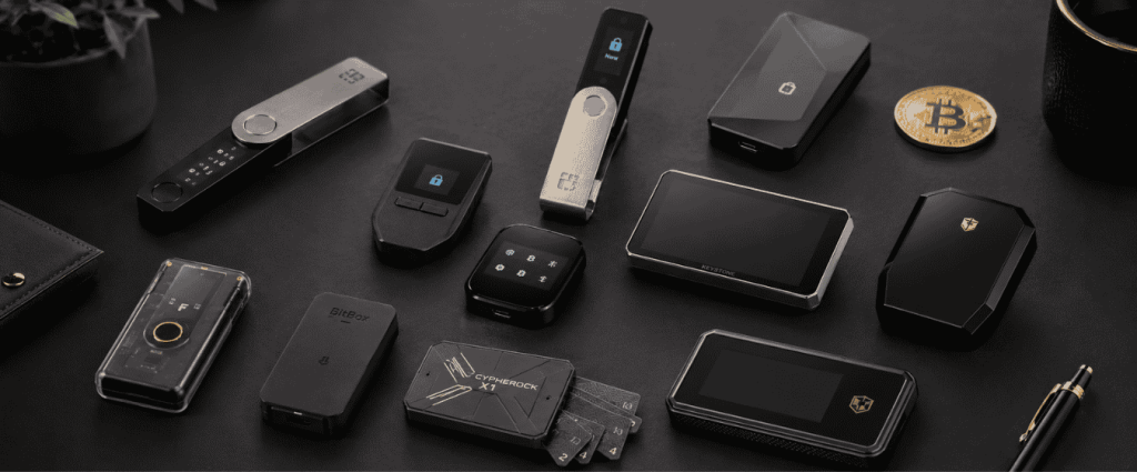 Collection of popular cryptocurrency hardware wallets displayed on a desk alongside a Bitcoin coin and tech accessories.